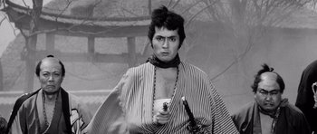 Movie still from “Yojimbo” (1961), directed by Akira Kurosawa – A man holding a sword in a black and white photo; Medium shot, Low angle