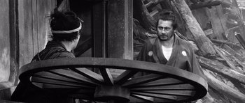 Movie still from “Yojimbo” (1961), directed by Akira Kurosawa – A man and a woman standing next to each other in front of a wooden structure; Medium shot, Over the shoulder angle