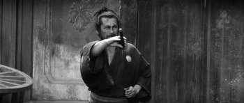 Movie still from “Yojimbo” (1961), directed by Akira Kurosawa – A man holding a gun in his hand; Medium shot, Low angle