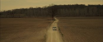 Movie still from “You're Next” (2011), directed by Adam Wingard – A car driving down a dirt road near a tree; Extreme Wide shot, High angle
