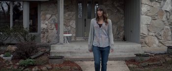 Movie still from “You're Next” (2011), directed by Adam Wingard – A woman standing in front of a stone house; Medium shot, Over the shoulder angle