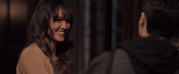 Movie still from “You're Next” (2011), directed by Adam Wingard – A woman smiles while sitting at a table; Close Up shot, Over the shoulder angle