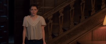 Movie still from “You're Next” (2011), directed by Adam Wingard – A young woman standing in front of a wooden staircase; Medium shot, High angle