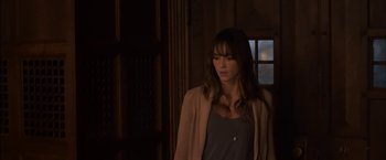 Movie still from “You're Next” (2011), directed by Adam Wingard – A woman standing in front of a window in the dark; Medium shot, Over the shoulder angle