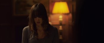 Movie still from “You're Next” (2011), directed by Adam Wingard – A woman is standing in front of a yellow lamp; Medium shot, Over the shoulder angle