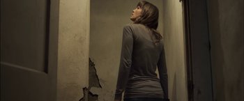 Movie still from “You're Next” (2011), directed by Adam Wingard – A woman standing in front of a cracked wall; Medium shot, Low angle
