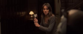Movie still from “You're Next” (2011), directed by Adam Wingard – A woman holding a hammer while standing in front of a lamp; Medium shot, Over the shoulder angle
