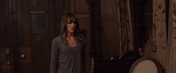 Movie still from “You're Next” (2011), directed by Adam Wingard – A woman standing in front of a wooden table; Medium shot, Over the shoulder angle