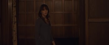 Movie still from “You're Next” (2011), directed by Adam Wingard – A woman standing in the dark in front of a wooden wall; Medium shot, Over the shoulder angle