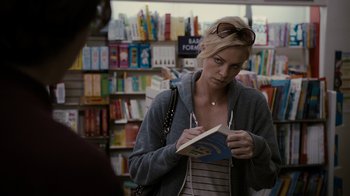 Movie still from “Young Adult” (2011), directed by Jason Reitman – A woman is reading a book in front of a bookcase; Medium shot, Over the shoulder angle