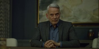 Movie still from “House of Cards” (2013), created by Beau Willimon – An older man sitting at a table in front of a painting; Close Up shot, Over the shoulder angle