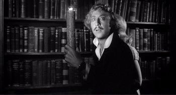 Movie still from “Young Frankenstein” (1974), directed by Mel Brooks – A man holding a candle in front of a bookshelf; Medium shot, Low angle