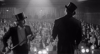 Movie still from “Young Frankenstein” (1974), directed by Mel Brooks – Two men in suits and top hats in front of an audience; Medium shot, Low angle