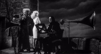 Movie still from “Young Frankenstein” (1974), directed by Mel Brooks – A man sitting on a chair next to two women; Wide shot, Low angle