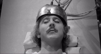 Movie still from “Young Frankenstein” (1974), directed by Mel Brooks – A man with a helmet on his head is laying on a bed; Close Up shot, High angle