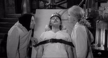 Movie still from “Young Frankenstein” (1974), directed by Mel Brooks – A man is strapped to a bed while two women look on; Medium shot, High angle