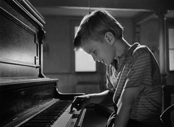 Movie still from “Young Man with a Horn” (1950), directed by Michael Curtiz – A young boy is playing the piano in a darkened room; Close Up shot, High angle