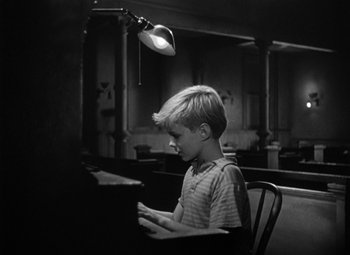 Movie still from “Young Man with a Horn” (1950), directed by Michael Curtiz – A young boy sitting at a table playing a piano; Medium shot, High angle