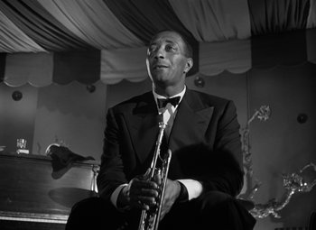 Movie still from “Young Man with a Horn” (1950), directed by Michael Curtiz – A black and white photo of a man in a suit holding a saxophone; Close Up shot, Low angle