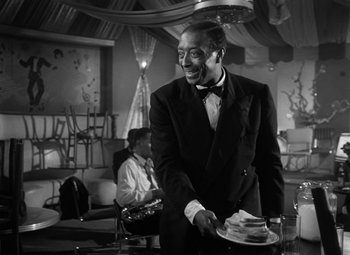 Movie still from “Young Man with a Horn” (1950), directed by Michael Curtiz – A black and white photo of a man holding a tray of food; Medium shot, Over the shoulder angle