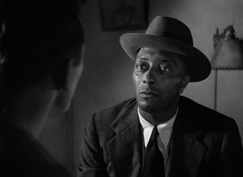 Movie still from “Young Man with a Horn” (1950), directed by Michael Curtiz – A black and white photo of a man wearing a suit and a hat; Close Up shot, Over the shoulder angle
