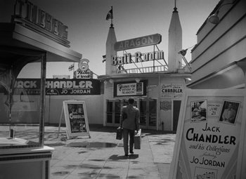 Movie still from “Young Man with a Horn” (1950), directed by Michael Curtiz – A man walking down the street holding a bag of luggage; Wide shot, High angle