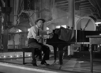Movie still from “Young Man with a Horn” (1950), directed by Michael Curtiz – A man sitting on a bench next to a grand piano; Wide shot, Low angle