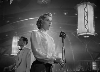 Movie still from “Young Man with a Horn” (1950), directed by Michael Curtiz – An old photo of a woman singing into a microphone; Medium shot, Low angle