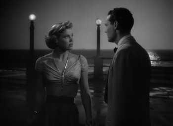 Movie still from “Young Man with a Horn” (1950), directed by Michael Curtiz – A man and a woman standing next to each other in front of lights; Medium shot, Low angle