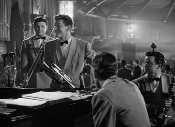 Movie still from “Young Man with a Horn” (1950), directed by Michael Curtiz – A group of men standing next to each other in a room; Medium shot, Over the shoulder angle