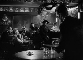 Movie still from “Young Man with a Horn” (1950), directed by Michael Curtiz – A group of people sitting at a table in a room; Wide shot, Over the shoulder angle