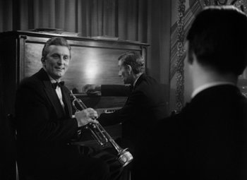 Movie still from “Young Man with a Horn” (1950), directed by Michael Curtiz – A man playing a trumpet in front of another man; Medium shot, High angle