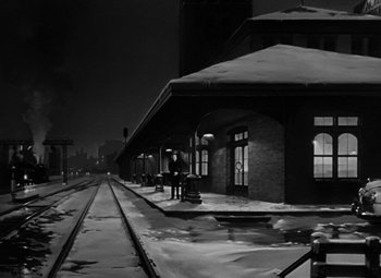 Movie still from “Young Man with a Horn” (1950), directed by Michael Curtiz – A man standing on a train platform next to snow covered ground; Extreme Wide shot, High angle