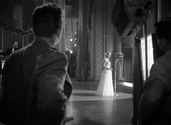 Movie still from “Young Man with a Horn” (1950), directed by Michael Curtiz – A woman in a white dress standing next to a man; Wide shot, Over the shoulder angle