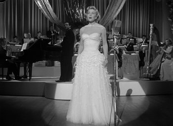 Movie still from “Young Man with a Horn” (1950), directed by Michael Curtiz – An old photo of a woman in a white dress singing; Wide shot, Low angle