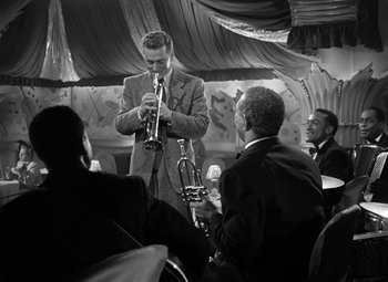 Movie still from “Young Man with a Horn” (1950), directed by Michael Curtiz – A black and white photo of a man playing the trumpet; Medium shot, Low angle
