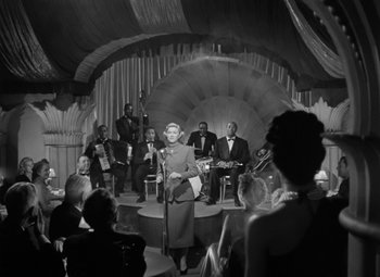 Movie still from “Young Man with a Horn” (1950), directed by Michael Curtiz – An old photo of a woman singing in front of an audience; Wide shot, Low angle