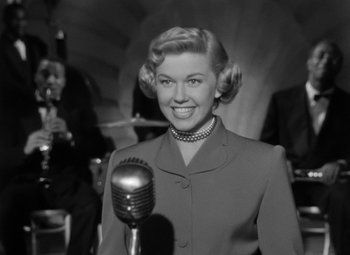 Movie still from “Young Man with a Horn” (1950), directed by Michael Curtiz – An old photo of a woman with a microphone in front of a band; Medium shot, Low angle
