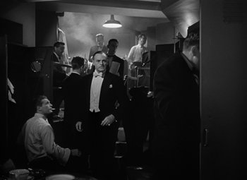 Movie still from “Young Man with a Horn” (1950), directed by Michael Curtiz – A group of men standing around in a room; Medium shot, Low angle