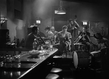 Movie still from “Young Man with a Horn” (1950), directed by Michael Curtiz – A black and white photo of a group of men sitting around a bar; Wide shot, High angle