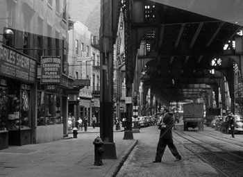 Movie still from “Young Man with a Horn” (1950), directed by Michael Curtiz – A black and white photo of a man walking down the street; Wide shot, Low angle