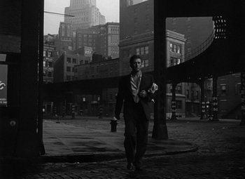 Movie still from “Young Man with a Horn” (1950), directed by Michael Curtiz – A black and white photo of a man in a suit walking on a city street; Wide shot, High angle