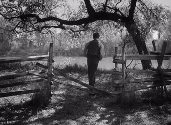 Movie still from “Young Mr. Lincoln” (1939), directed by John Ford – A man standing next to a tree near a wooden fence; Wide shot, High angle