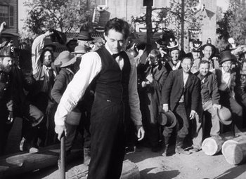 Movie still from “Young Mr. Lincoln” (1939), directed by John Ford – An old black and white photo of a man holding a baseball bat in front of a crowd; Medium shot, Over the shoulder angle