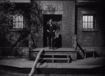 Movie still from “Young Mr. Lincoln” (1939), directed by John Ford – A black and white photo of a man standing in front of a brick building; Wide shot, Low angle
