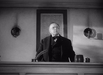 Movie still from “Young Mr. Lincoln” (1939), directed by John Ford – An older man sitting at a desk in front of a clock; Medium shot, Low angle