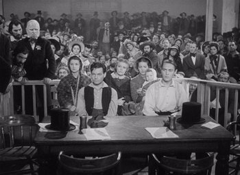 Movie still from “Young Mr. Lincoln” (1939), directed by John Ford – A group of people sitting at a table in front of a crowd of onlookers; Wide shot, High angle
