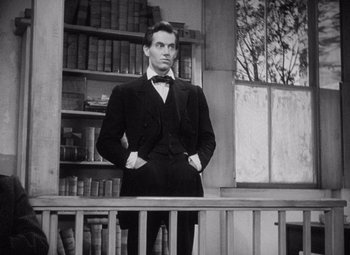 Movie still from “Young Mr. Lincoln” (1939), directed by John Ford – A black and white photo of a man standing in front of bookshelves; Medium shot, Over the shoulder angle