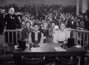 Movie still from “Young Mr. Lincoln” (1939), directed by John Ford – A group of people sitting at a table in front of an audience; Wide shot, High angle