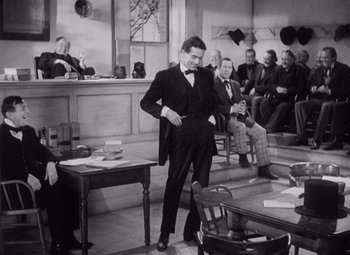 Movie still from “Young Mr. Lincoln” (1939), directed by John Ford – An old photo of a man in a suit and bow tie in front of a group of people; Wide shot, Over the shoulder angle